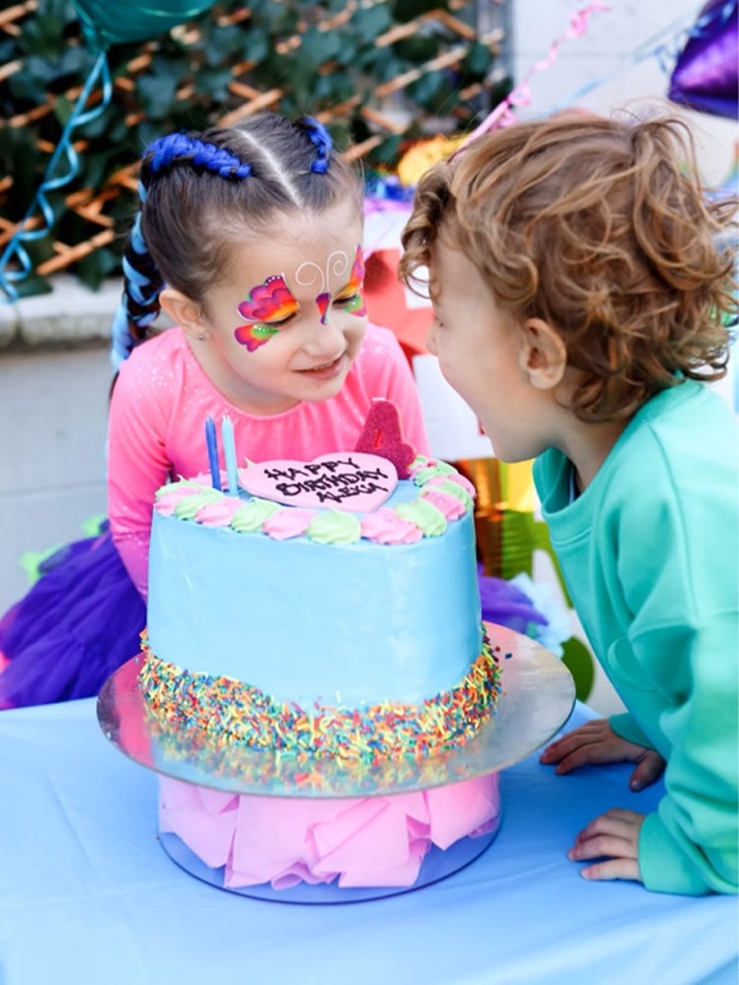 Two children smiling in front of a birthday cake at a ColorBloom art party